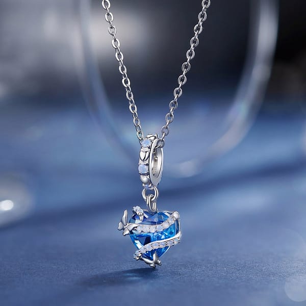 Buzzworthy Beauties: 10 Must-Have Bug-Inspired Jewelry Pieces of 2023 20 Cinderella Magic Glass Heart Dangle Charm crafted from s925 sterling silver, featuring a blue glass heart wrapped in opal-adorned silver swirls with butterfly accents.