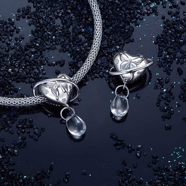 Buzzworthy Beauties: 10 Must-Have Bug-Inspired Jewelry Pieces of 2023 28 Close-up of the Butterfly Heart Planet Charm made of s925 sterling silver. Features an engraved silver butterfly on a heart, with a planet-like ring and a dangling transparent glass drop. Part of the Parallel Universe Charms Collection. Perfect for jewelry lovers and dreamers.