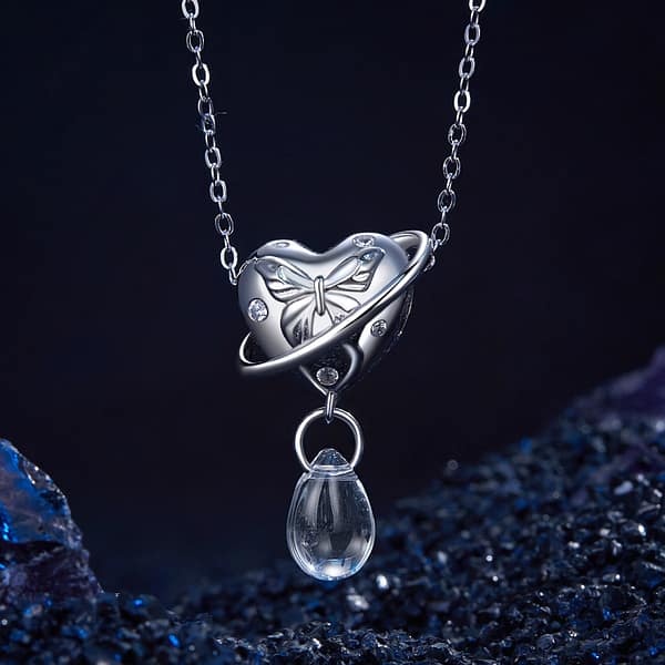 Buzzworthy Beauties: 10 Must-Have Bug-Inspired Jewelry Pieces of 2023 30 Close-up of the Butterfly Heart Planet Charm made of s925 sterling silver. Features an engraved silver butterfly on a heart, with a planet-like ring and a dangling transparent glass drop. Part of the Parallel Universe Charms Collection. Perfect for jewelry lovers and dreamers.